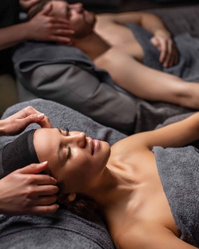 side view on couple getting face and head treatment. relaxed couple lying down on massage bed during facial treatment at asian spa and wellness center